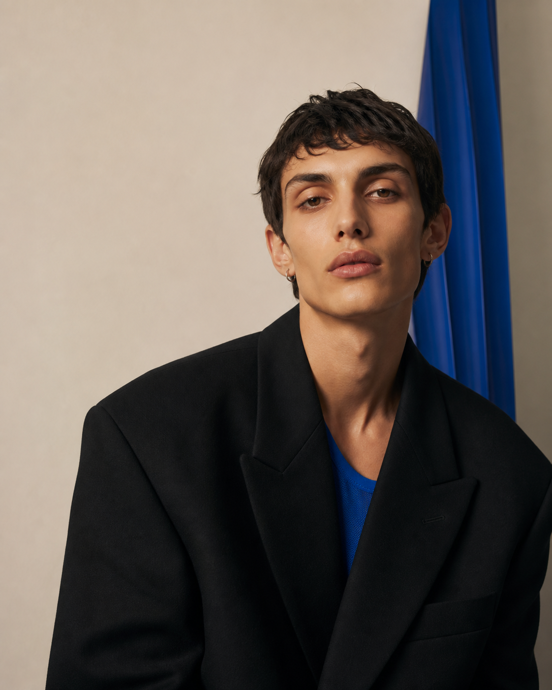 Conceptual editorial portrait of an androgynous young fashion model in a black tailored jacket with cobalt blue accents